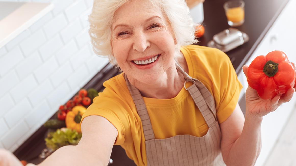 Uśmiechnięta, siwowłosa pani trzyma w ręku paprykę