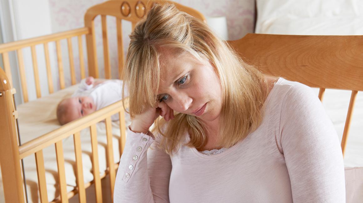 Smutna matka, w tle niemowlę w łóżeczku