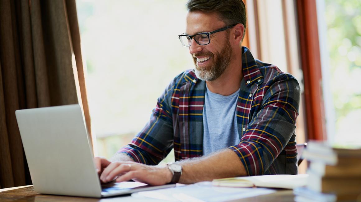 Uśmiechnięty brodaty 40-latek przed komputerem