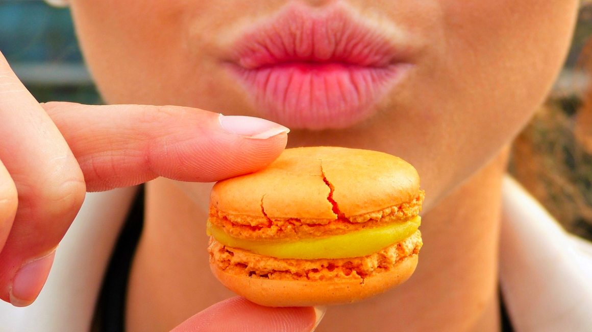 Widok dolnej części twarzy i ciasta przed nią trzymanego dwoma pacami prawej ręki. Ciastko z nadzieniem w środku.