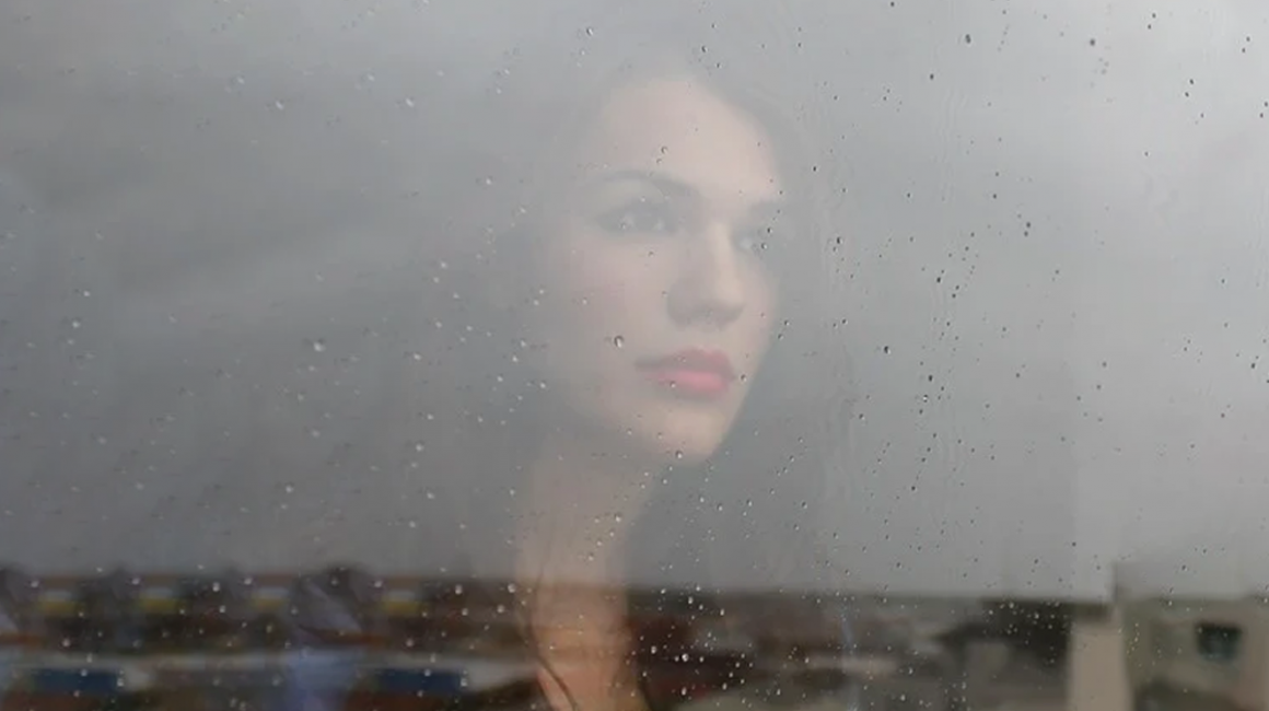 Twarz kobiety stojącej za zamgloną szybą.