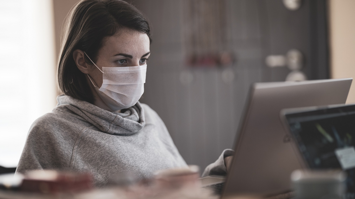 Kobieta w maseczce siedząca przed komputerem.