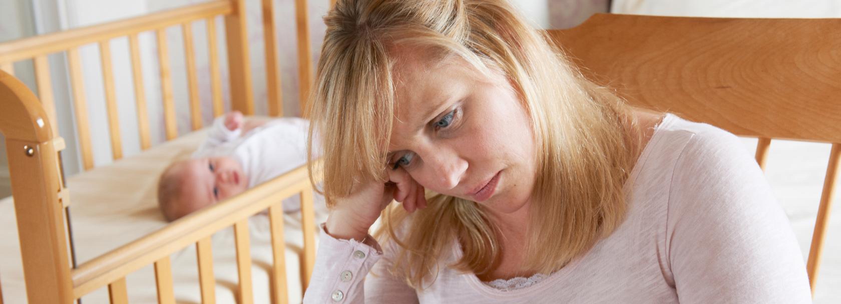 Smutna matka, w tle niemowlę w łóżeczku