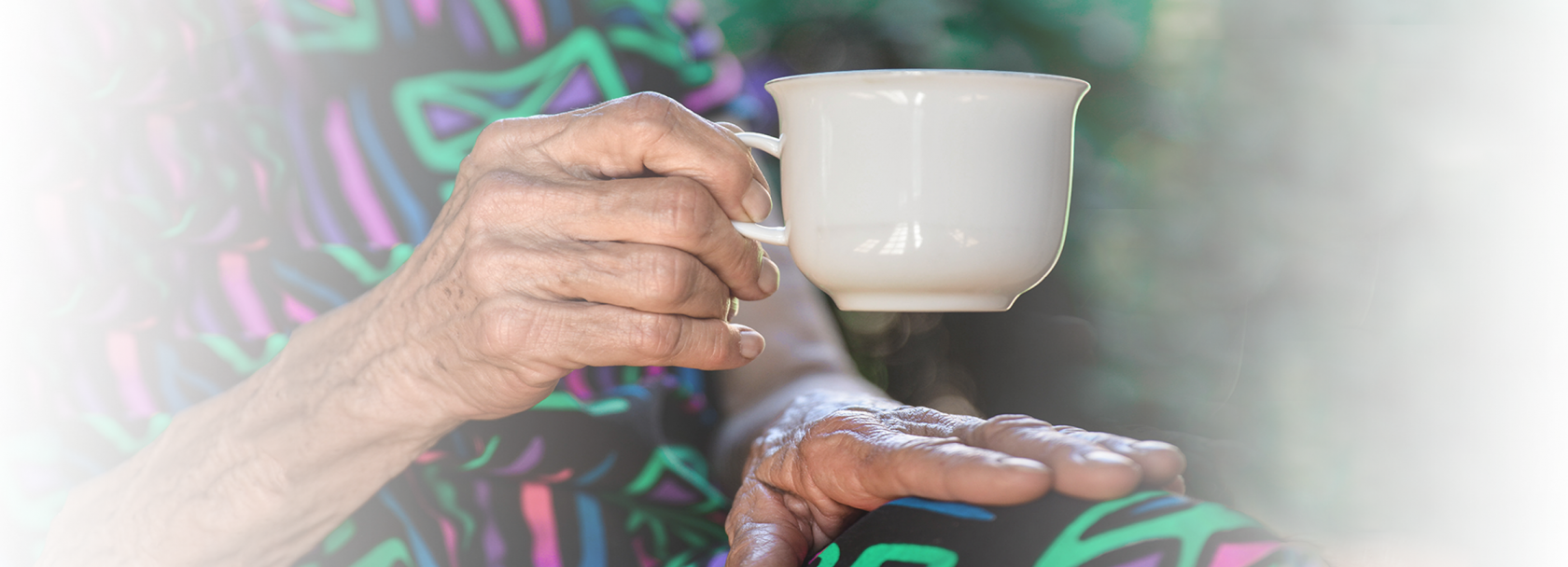 Wykadrowana starsza kobieta, która siedzi i w prawej ręce trzyma filiżankę. Widać ręce, filiżankę i fragment tułowia.