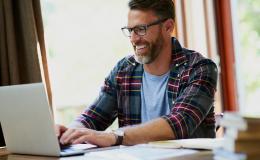 Uśmiechnięty brodaty 40-latek przed komputerem