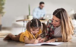 Córka rysuje, matka leży obok, w tle ojciec z komputerem