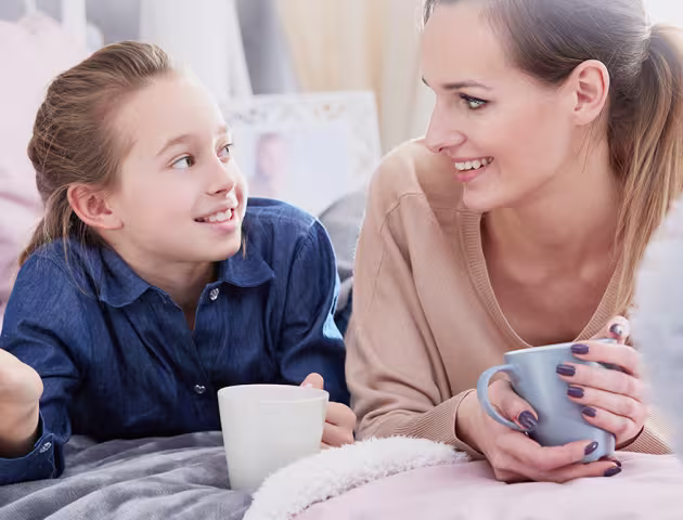 Mama i córka leżą na łóżku z herbatą i rozmawiają