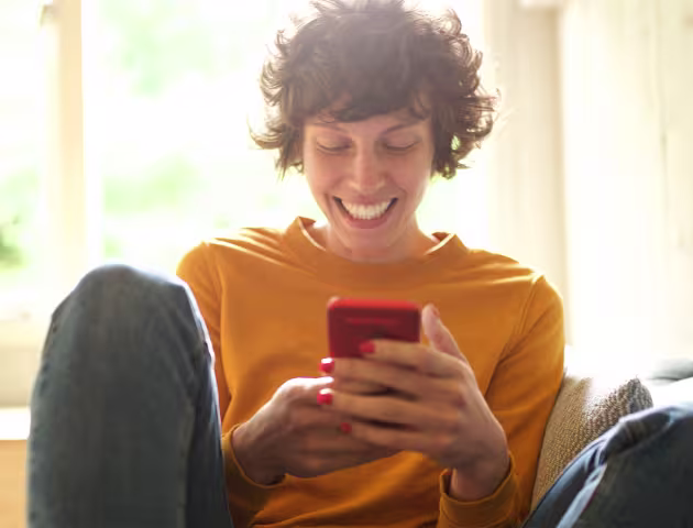 Roześmiana dziewczyna trzyma w ręku telefon i patrzy na ekran