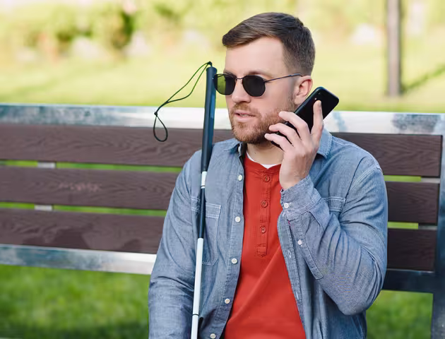 niewidomy mężczyzna z telefonem na ławce