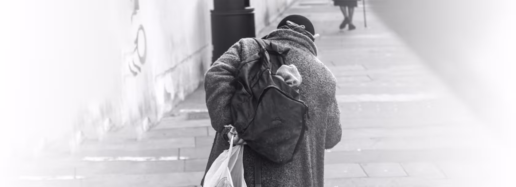 Bezdomna osoba z plecakiem i reklamówką, od tyłu, wchodząca po schodach