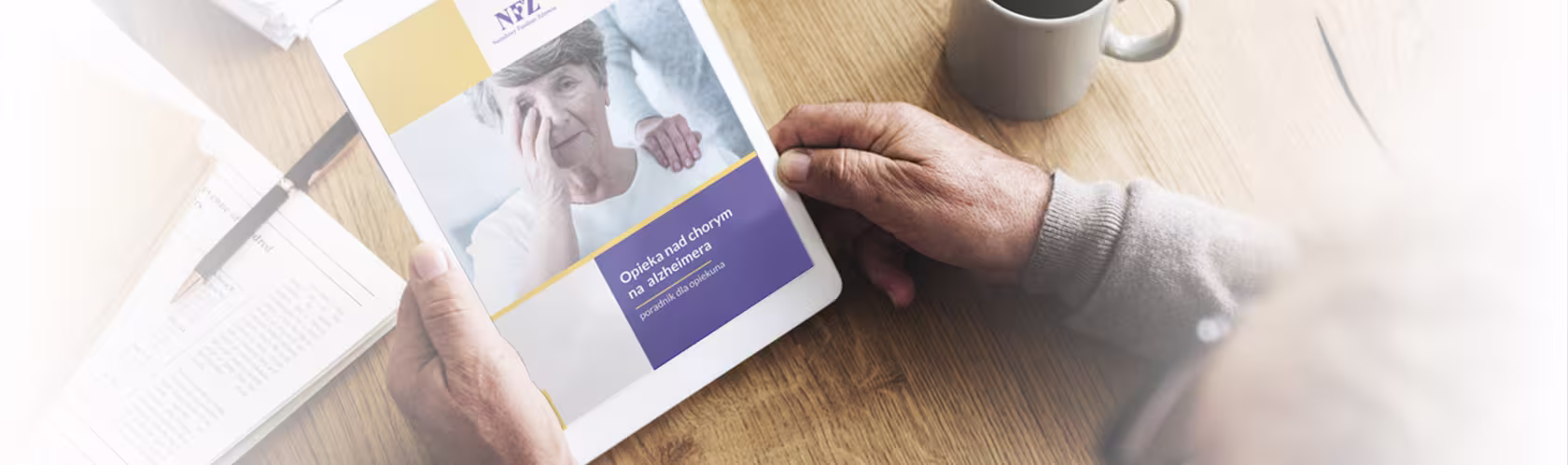 Mężczyzna trzyma w rękach tablet. Ma na nim wyświetlony poradnik dla opiekunów nad chorym na alzheimera