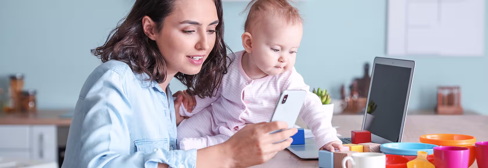 Mama z dzieckiem przy stole. Mama przegląda telefon, a dziecko bawi się klockami.