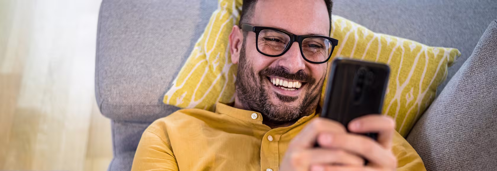 Mężczyzna w żółtej koszuli leży na kanapie z telefonem