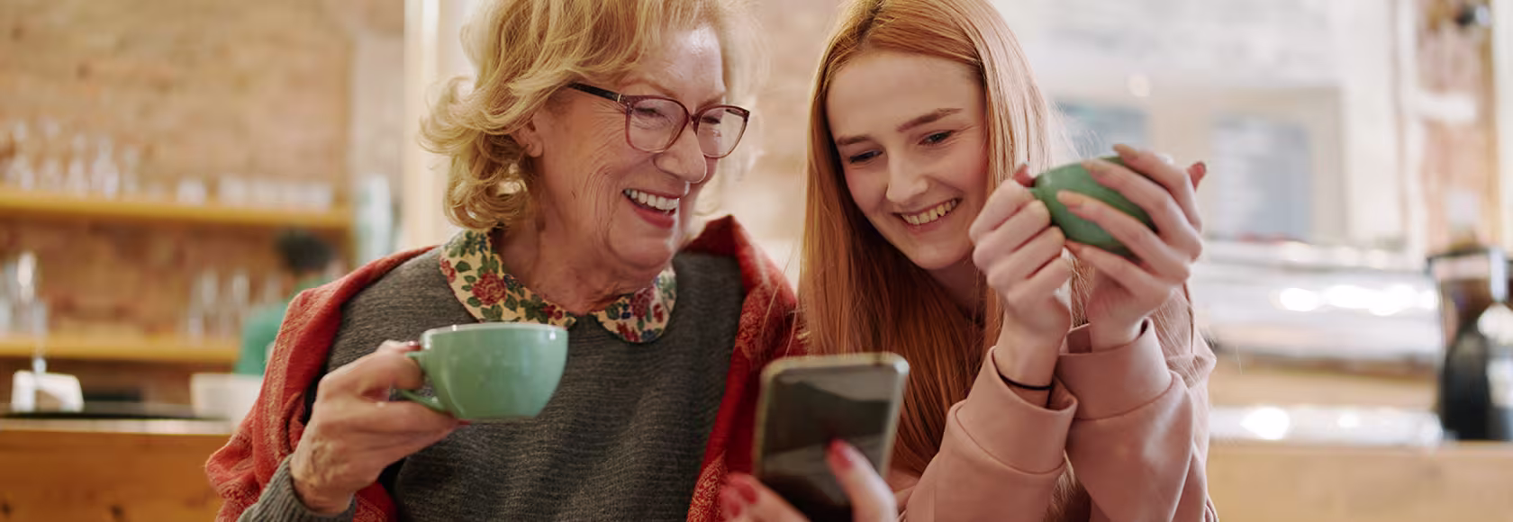 Babcia i wnuczka patrzą na telefon komórkowy, pijąc herbatę w kuchni