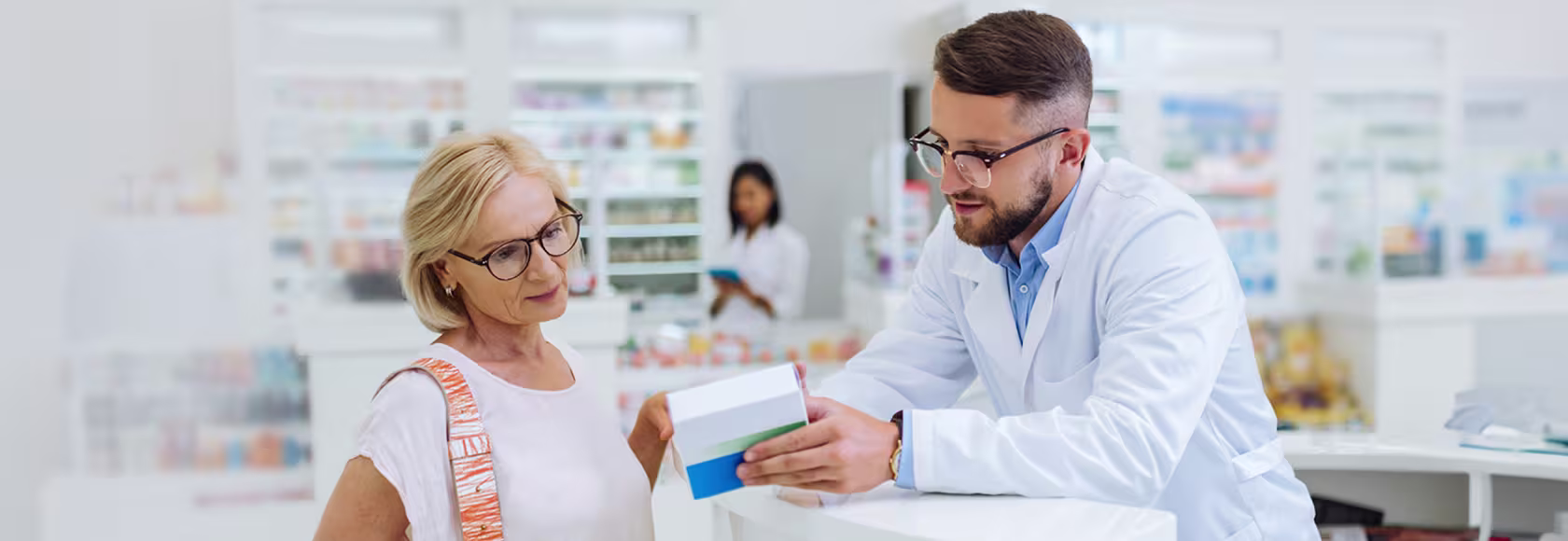 farmaceuta tłumaczy coś starszej pacjentce z lekiem w ręku
