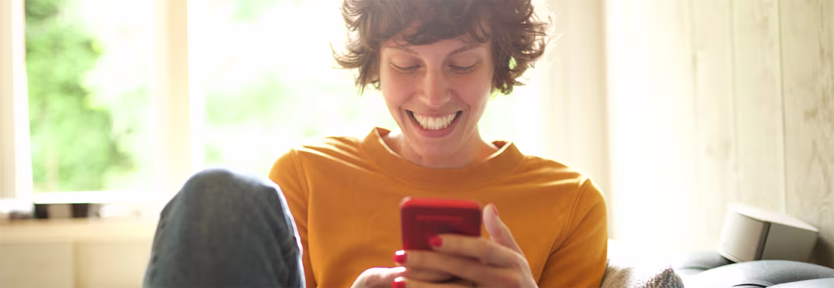Roześmiana dziewczyna trzyma w ręku telefon i patrzy na ekran