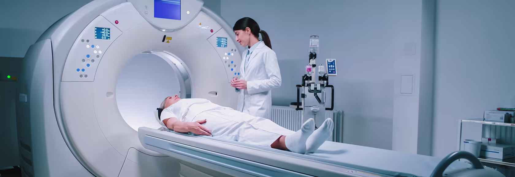 osoba leży na łóżku tomografu, obok stoi pielęgniarka